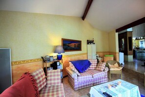 A living room with a sofa, armchairs, a table with architectural plans, and a painting on the wall.