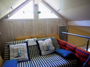 Una habitación con techo inclinado, una cama con ropa de cama a rayas y un ventanal que proporciona luz natural.