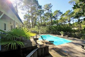 A wooden deck with a swimming pool, surrounded by trees and a house. - House with pool and terrace facing the Golf G0275 (Lacanau-Ocean)