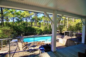 A covered outdoor swimming pool area with a wooden deck, lounge chairs, and a view of a forested area. - House with pool and terrace facing the Golf G0275 (Lacanau-Ocean)