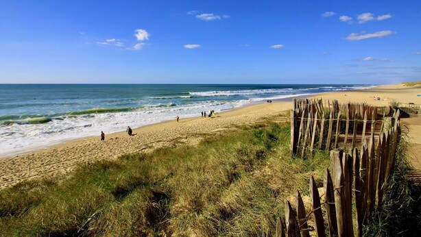 Une plage avec une clôture en bois, un rivage sablonneux et des vagues de l’océan.