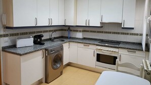 Une cuisine compacte avec des meubles blancs, un lave-linge, un grille-pain et un évier.