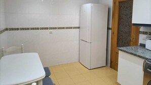 Une cuisine de taille réduite avec des carreaux blancs, un réfrigérateur blanc, une porte en bois et un plan de travail en granit.