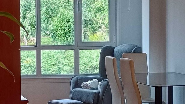 Une chambre moderne dotée d’une grande fenêtre, d’un canapé, d’un fauteuil et d’un petit pouf.