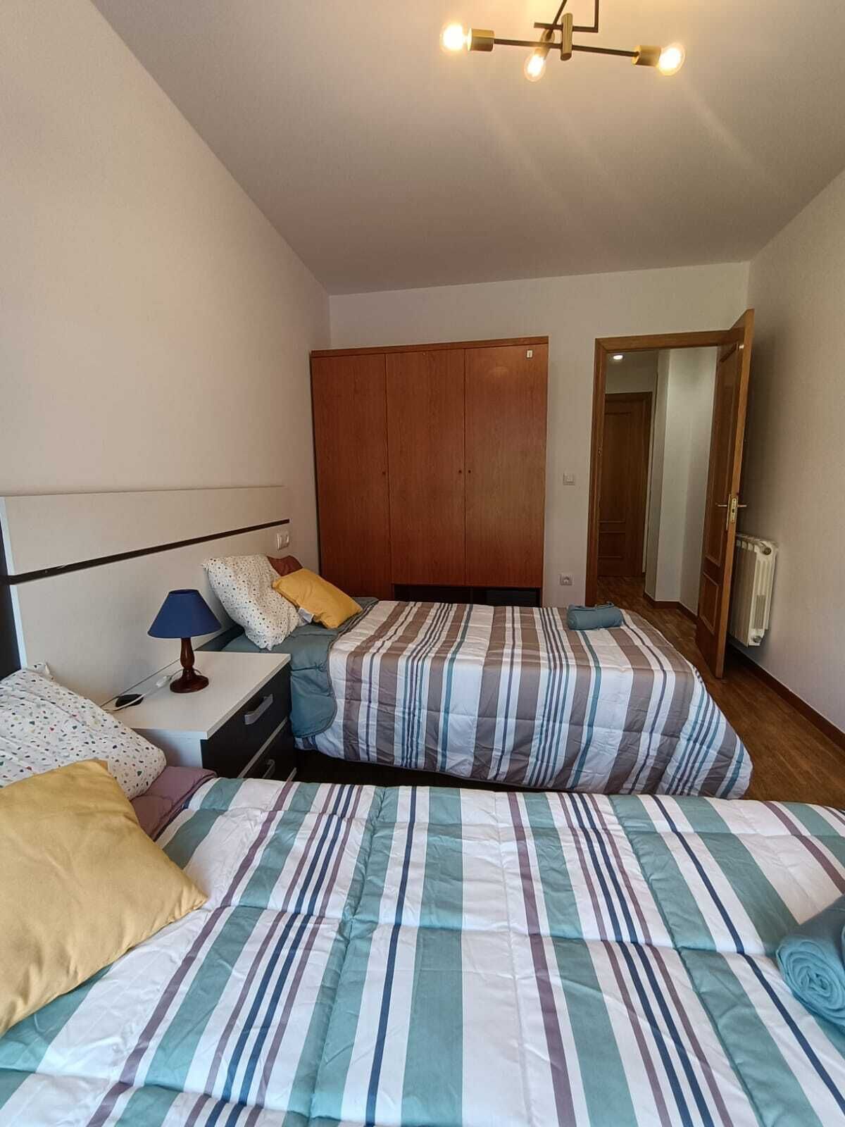 Un dormitorio con dos camas, un armario de madera, una mesita de noche con lámpara y un espejo.