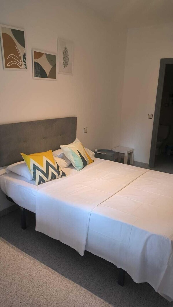 A neatly made bed with a grey headboard, a bedside table, and abstract wall art.