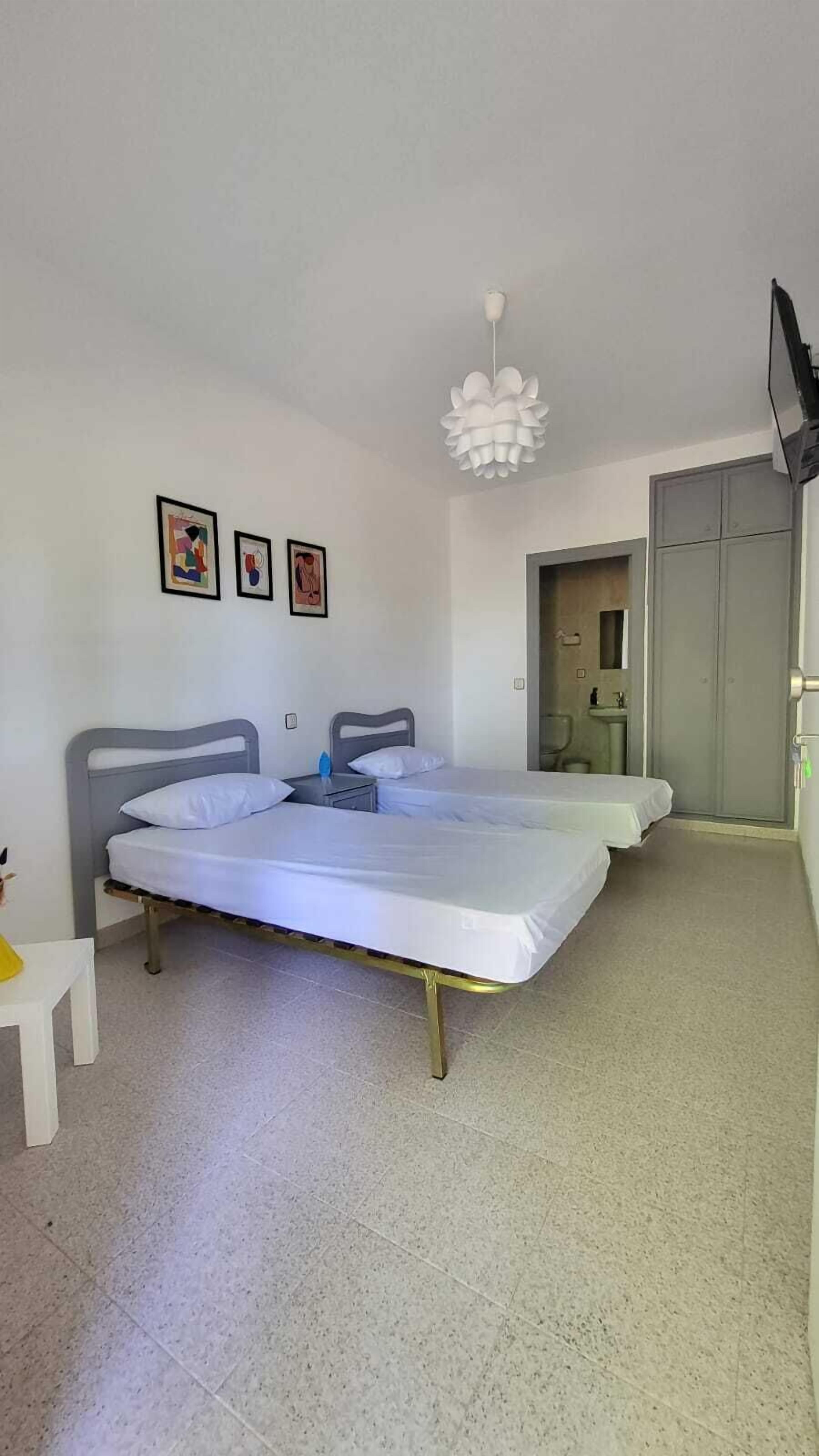 Une chambre avec deux lits, un bureau blanc et une salle de bain visible à travers une porte ouverte.