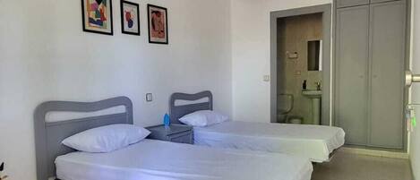 Una habitación con dos camas, un escritorio blanco y un baño que se ve a través de una puerta abierta.