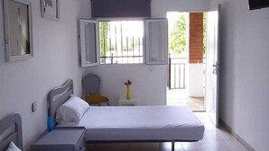 A bedroom with two beds, a small table, a chair, a TV, and a window with a view of the outside. - Hostal San Martin de Montalbán (San Martin de Montalban)