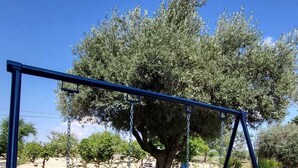 A swing set with two wooden seats and a metal frame, located in a park with a large tree in the background. - Hostal San Martin de Montalbán (San Martin de Montalban)