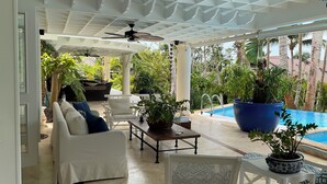 A covered outdoor seating area with white furniture, a pool, and lush greenery. - "srvittinivillas Lc01  Resorts / Spacious/ Family/ Group/ Best Loc" (La Romana)