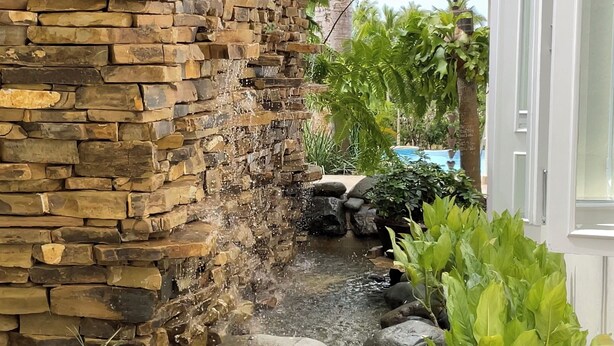 A stone wall with a small stream flowing through it, surrounded by lush greenery and a pool in the background. - "srvittinivillas Lc01  Resorts / Spacious/ Family/ Group/ Best Loc" (La Romana)
