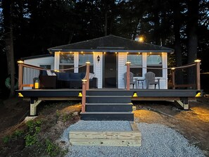 A wooden deck with a covered seating area, a small table, and chairs. - Lakefront Cottage On Beautiful Maine Lake (Buxton)