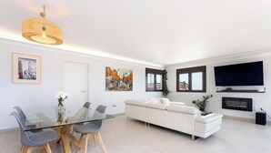 Un salon moderne avec une table à manger en verre, un canapé blanc et un téléviseur à écran plat fixé au mur.