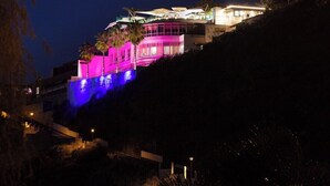 Un bâtiment moderne abritant un restaurant à l’étage supérieur, illuminé de couleurs vives, notamment du rose et du bleu.