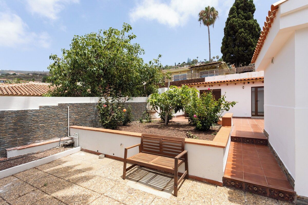 Une terrasse avec un banc en bois, un sol carrelé et un mur blanc avec une fenêtre.