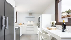Une cuisine moderne avec des meubles blancs, un four encastré et une fenêtre donnant sur un quartier résidentiel.