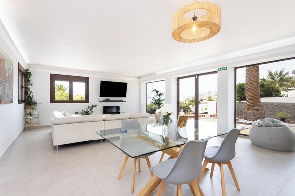 A modern living room with a glass dining table, white sofa, and a television.