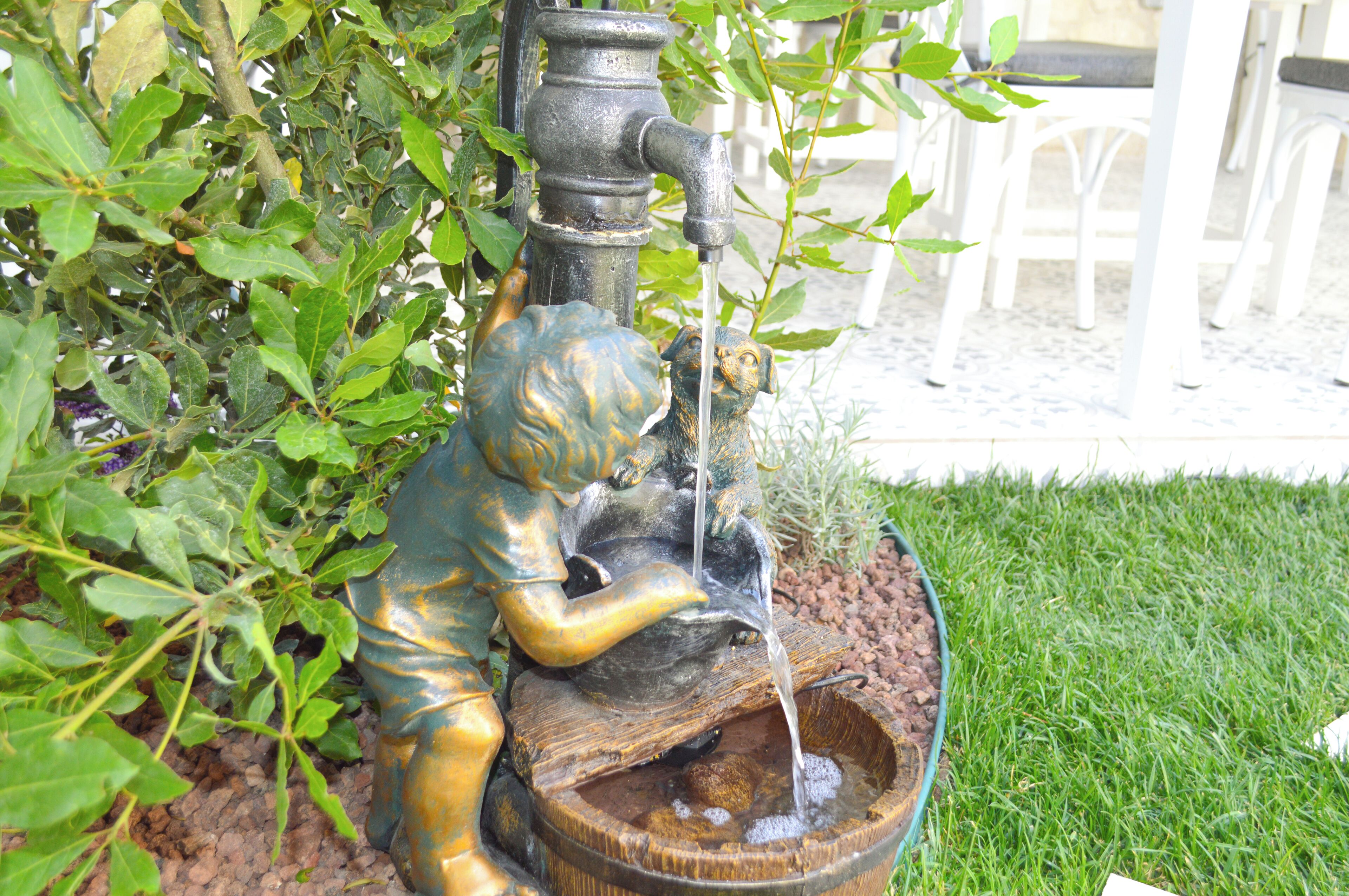 A garden with a bronze statue of a child and a water fountain.