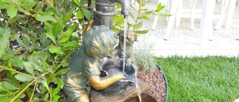 A garden with a bronze statue of a child and a water fountain.