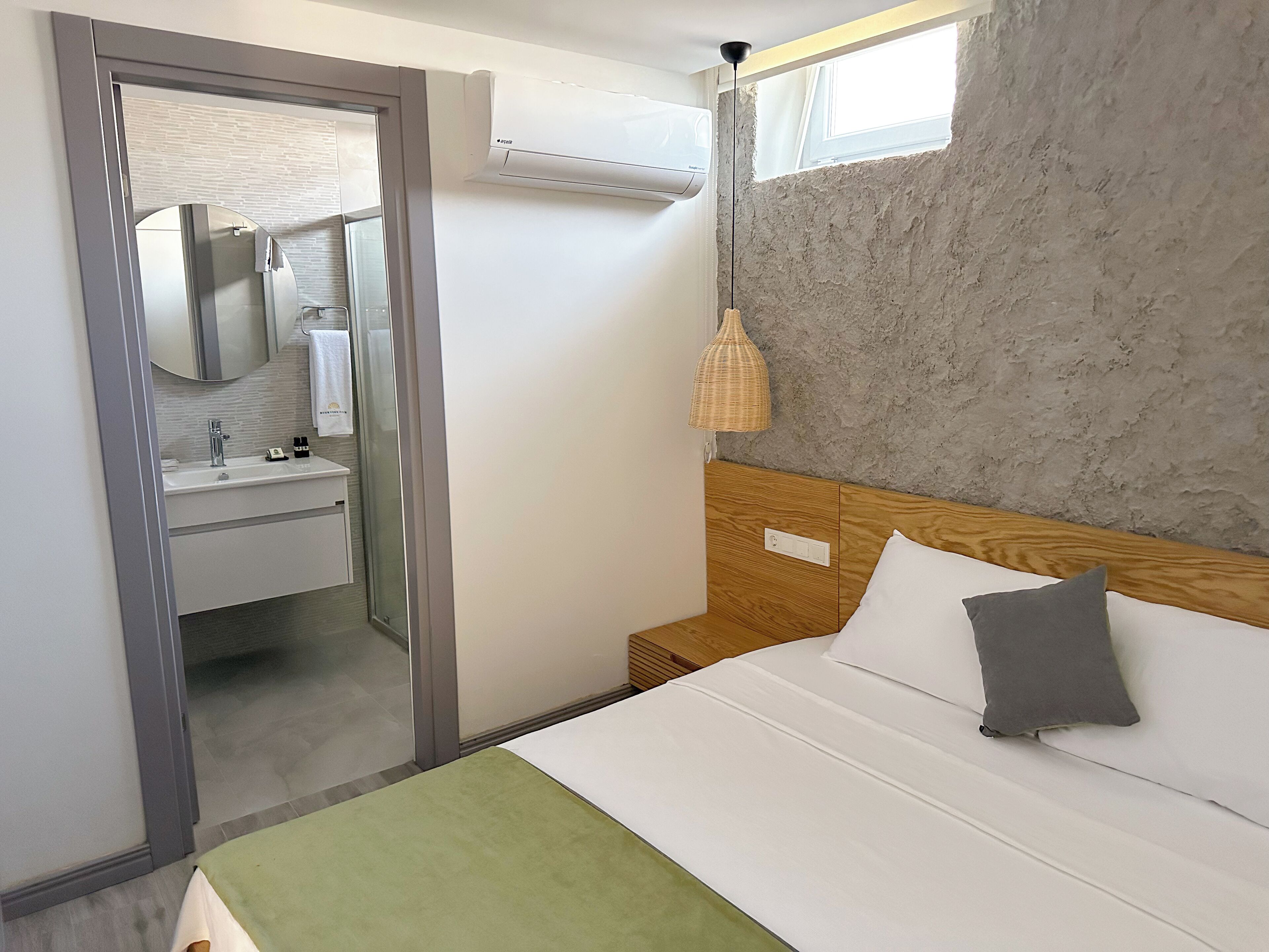 A modern hotel room with a bed, a bedside table, a mirror, and a bathroom visible through an open door.