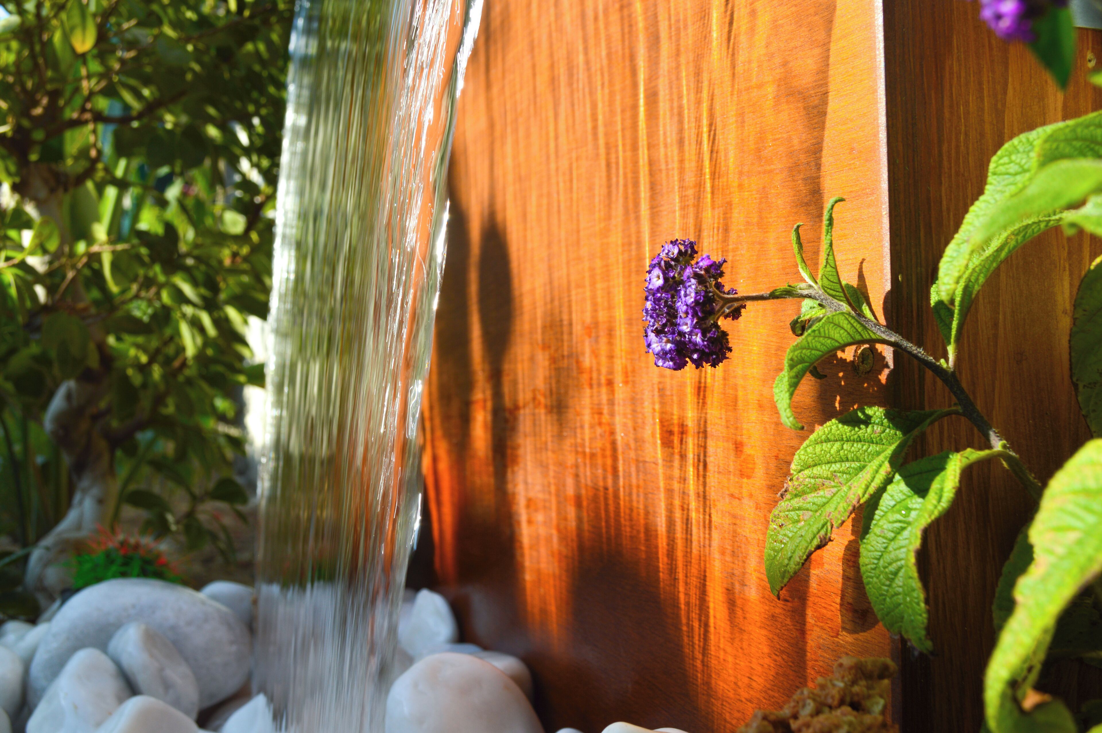 Una cerca de madera con una cascada pequeña y una flor morada.
