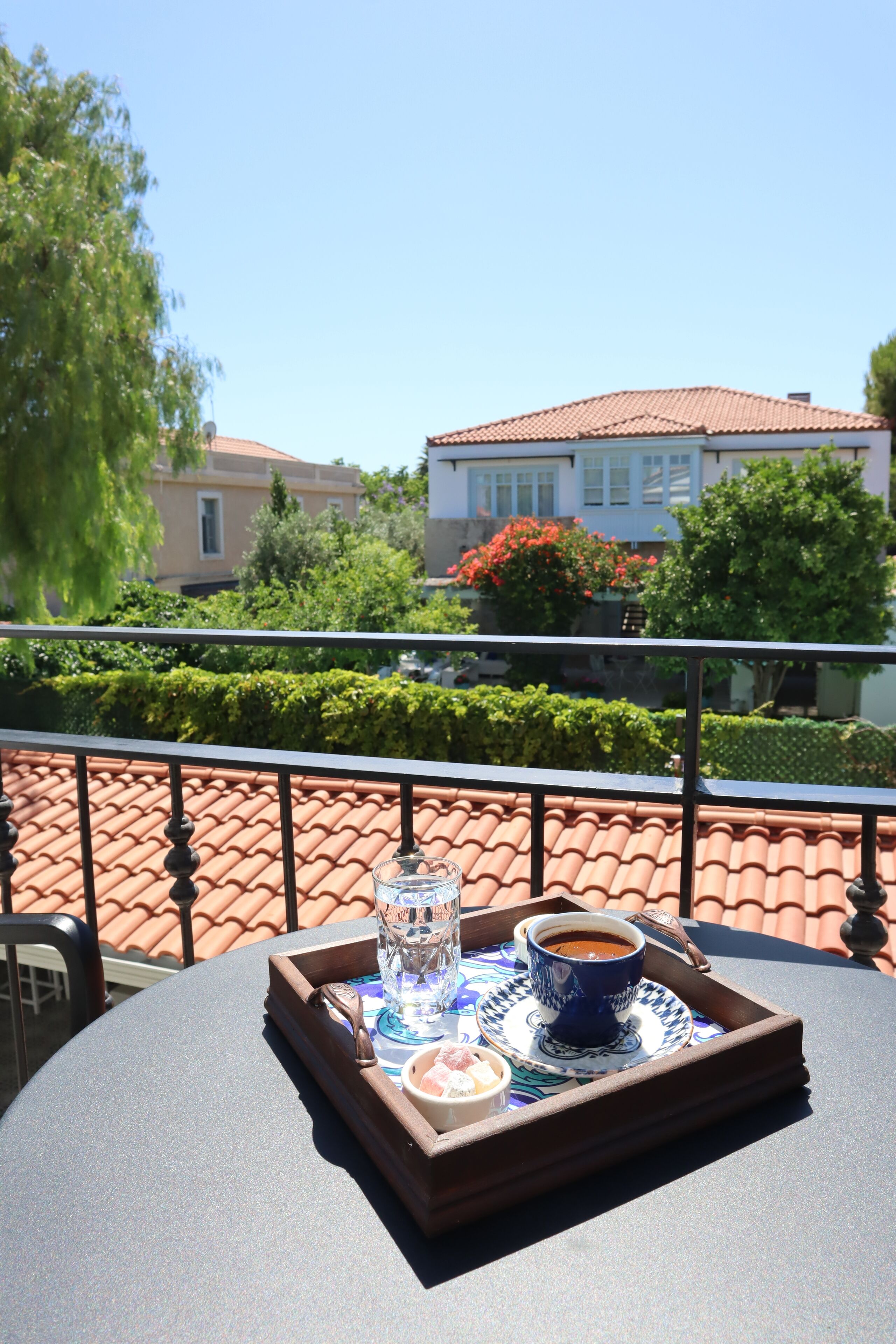 Eine Terrasse mit Tisch, gedeckt für Getränke und einen kleinen Imbiss, mit Blick auf einen Garten und ein Gebäude mit einem Ziegeldach.