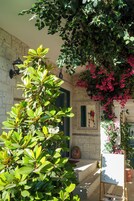 Un edificio de piedra con una puerta verde, un caballete blanco con un dibujo y abundante follaje verde.