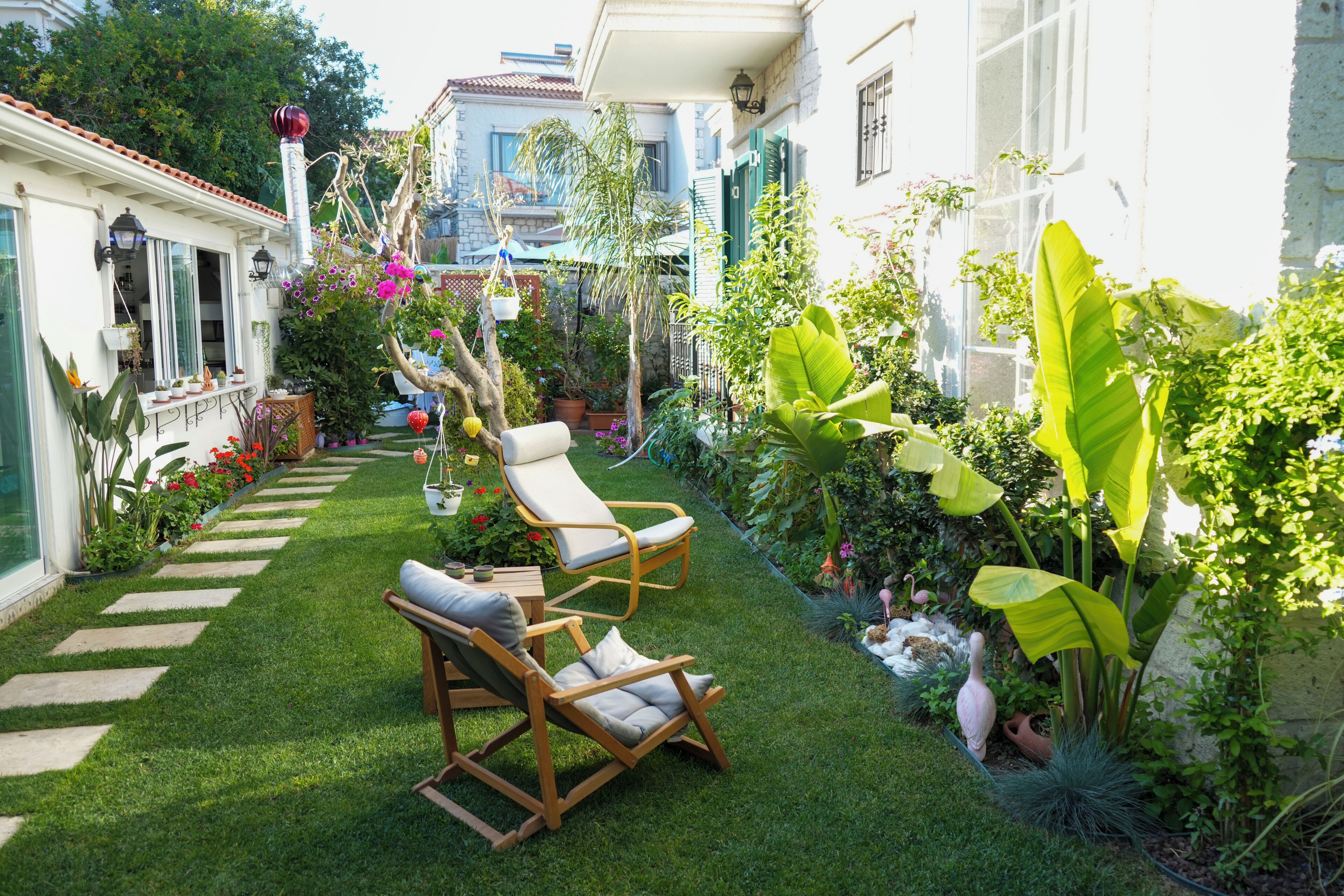 Un jardín bien cuidado con césped, dos mecedoras de madera y diversas plantas en macetas.