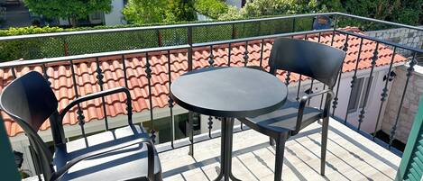 A balcony with a round table and two chairs, overlooking a courtyard with trees and buildings.