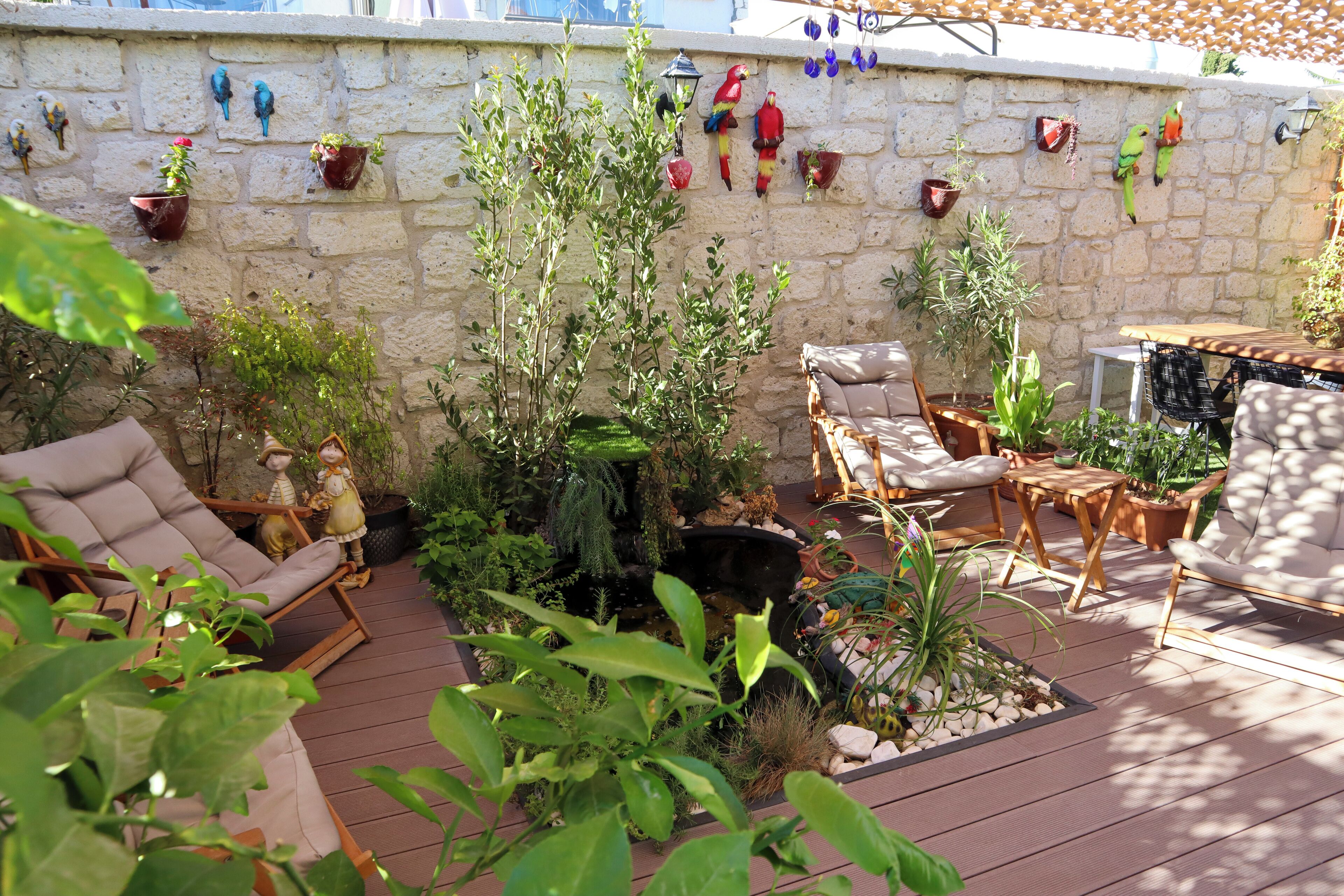 A patio with outdoor furniture, a stone wall with hanging birdhouses, and various potted plants.