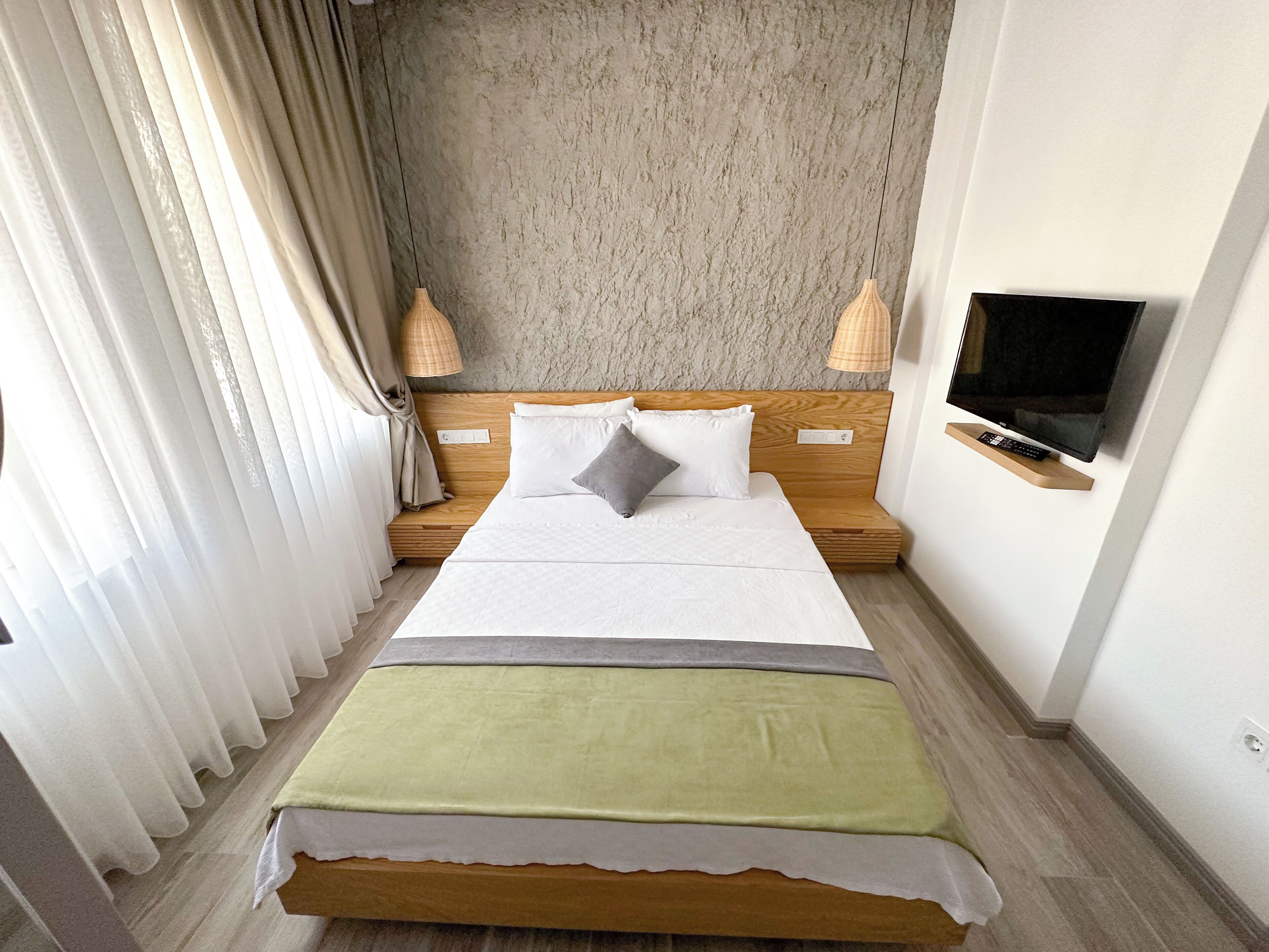 A hotel room with a bed, curtains, a television, and a wall-mounted shelf.