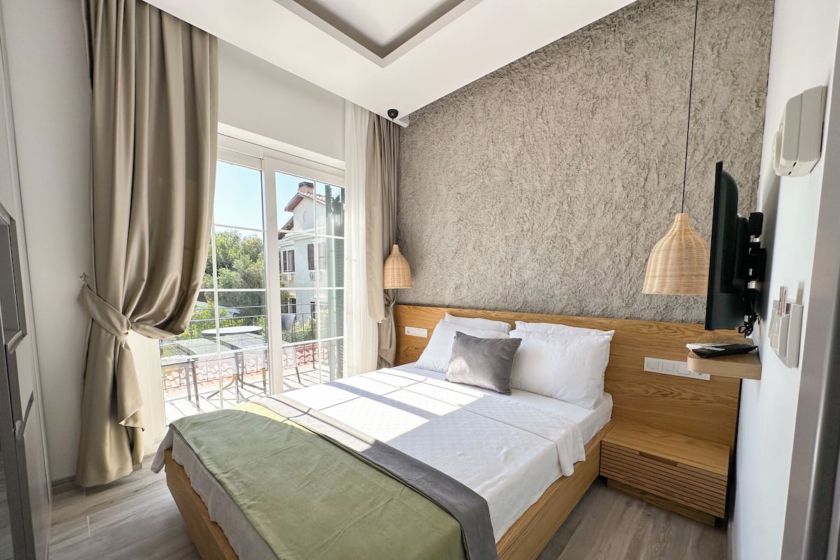 Une chambre moderne avec un grand lit, une tête de lit en bois, un balcon avec une table et un mur à texture.