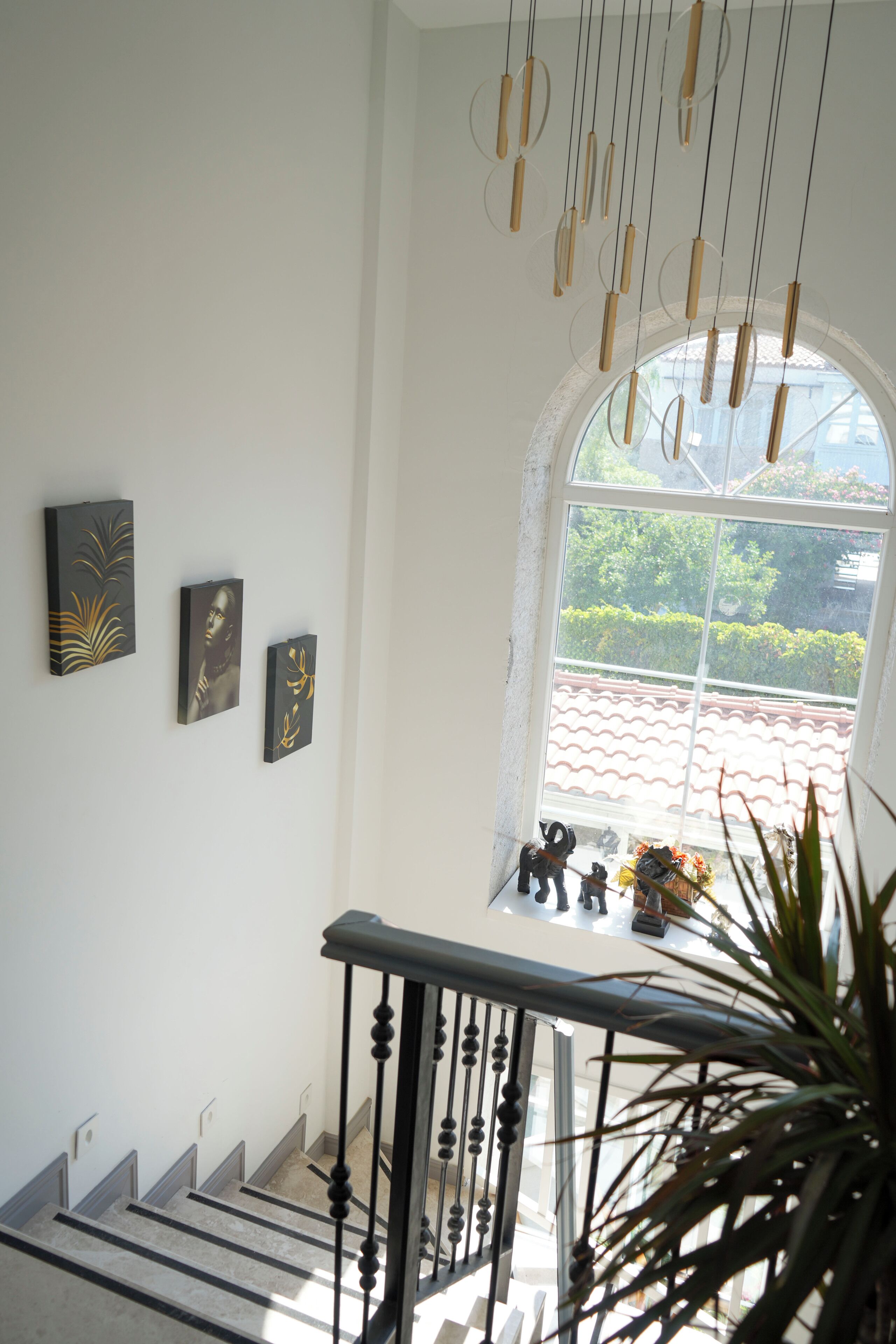Una escalera con barandilla negra, un candelabro colgante y tres cuadros en la pared.