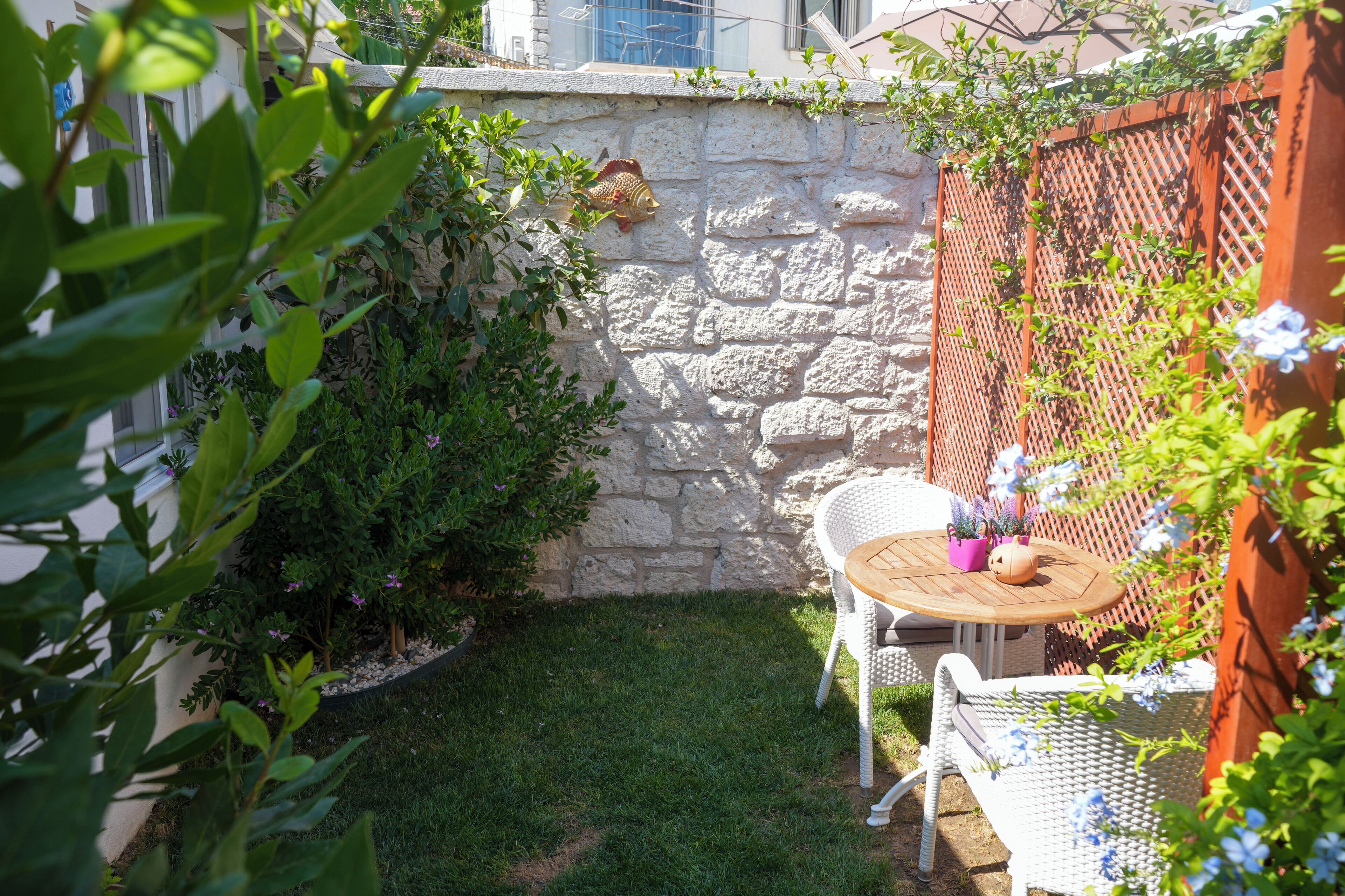 A stone wall with climbing plants, a small round wooden table with chairs, and a potted plant.