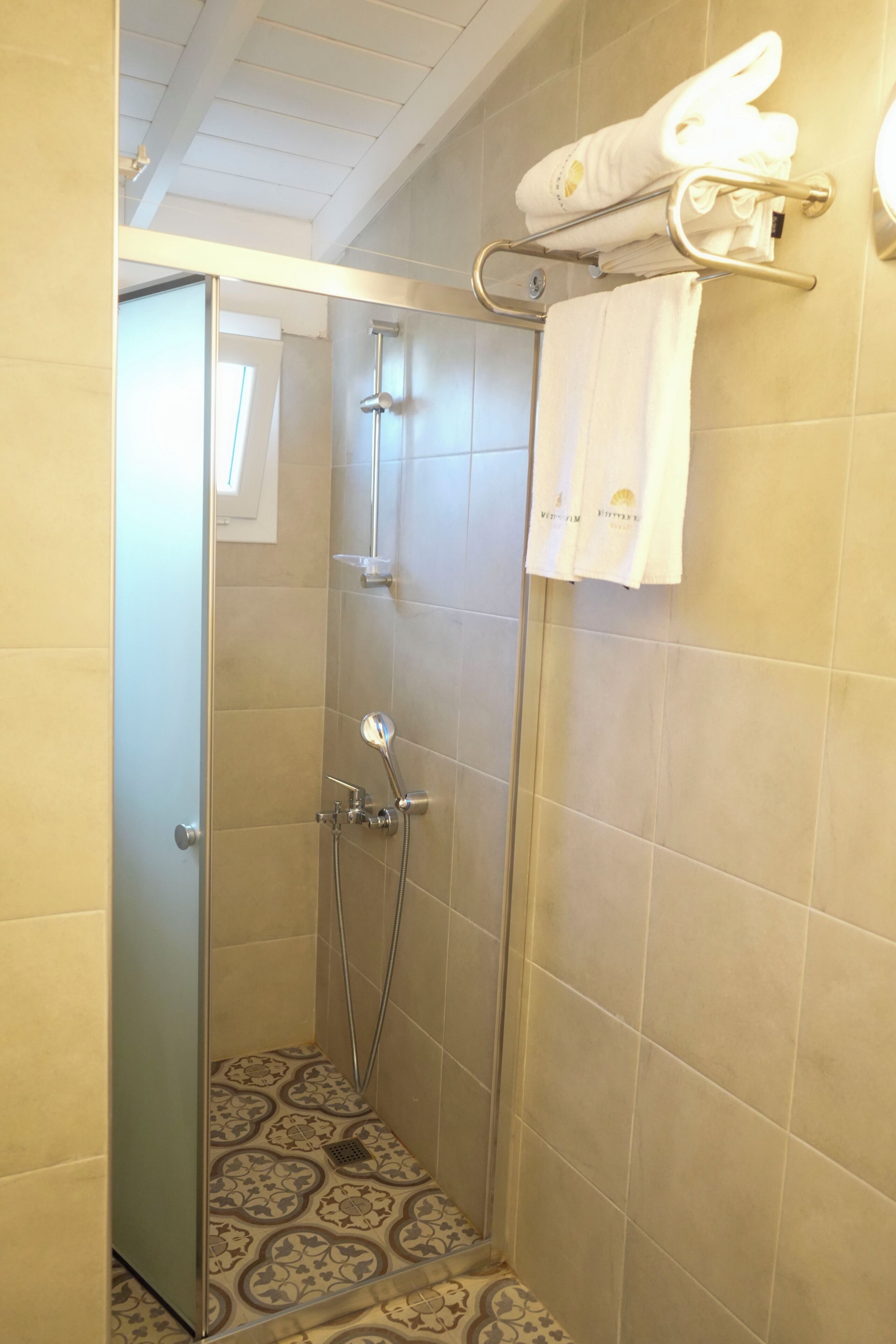 Eine Dusche mit Glastür, ein Handtuchhalter mit Handtüchern und geflieste Böden mit Muster.