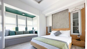 Ein Schlafzimmer mit einem großen Bett, einer Sitzbank unter dem Fenster mit Kissen, einem Nachttisch und einer Lampe.