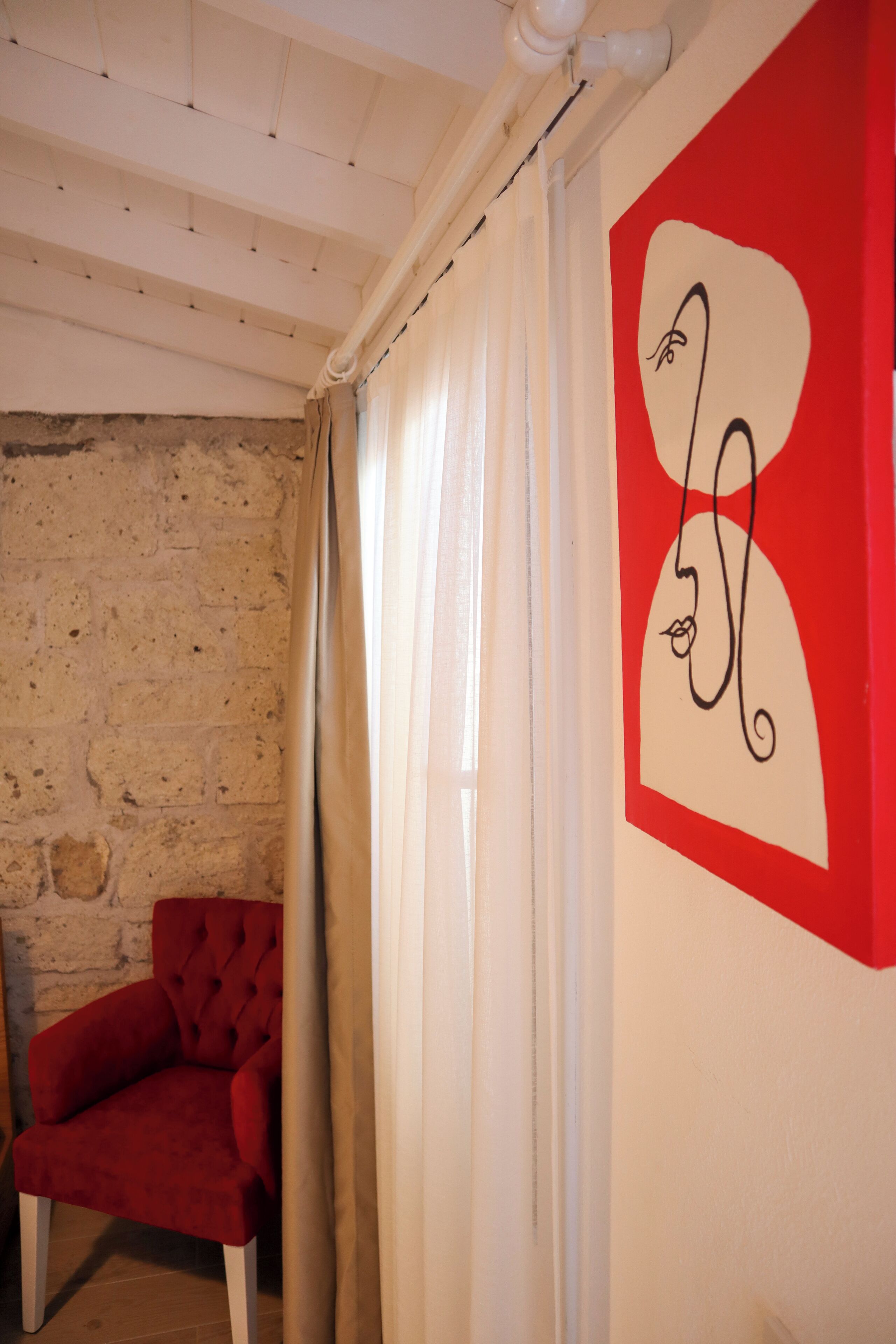 Una habitación con una silla roja, una pared blanca con un diseño abstracto rojo y blanco, y una pared de piedra.