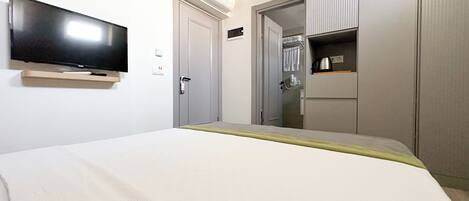 A hotel room with a bed, a flat-screen TV mounted on the wall, a wardrobe, and a small kitchenette area.