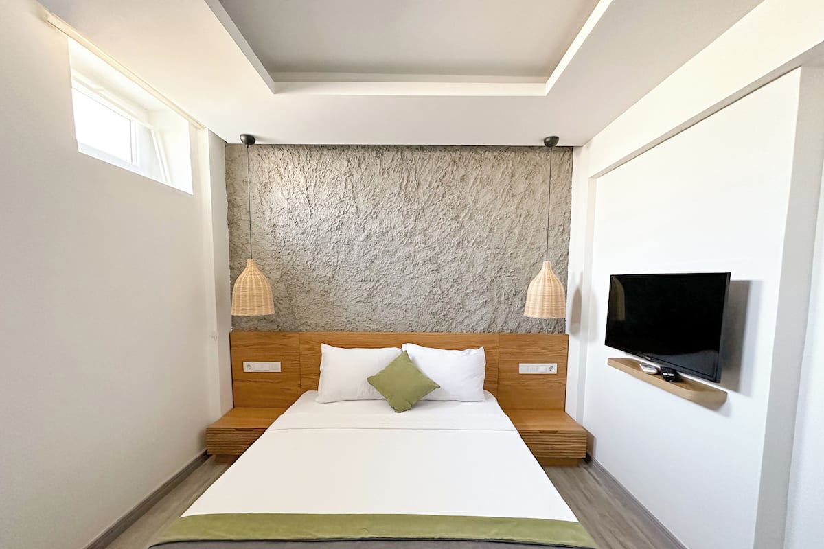 Une chambre d’hôtel moderne avec un grand lit, un téléviseur fixé au mur et deux lampes suspendues.
