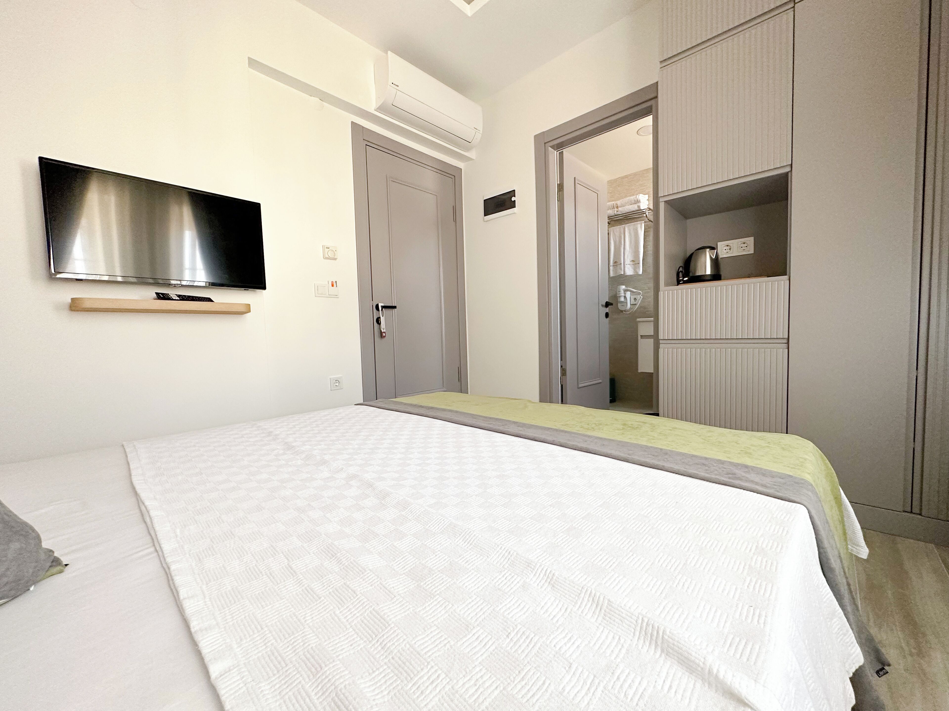 A hotel room with a bed, a TV mounted on the wall, a wardrobe, and a bathroom visible through an open door.