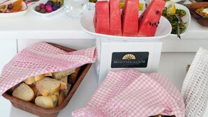 Ein Tisch ist reichhaltig mit Speisen gedeckt, darunter Brot, Wassermelone und verschiedene kleine Schüsseln und Teller.