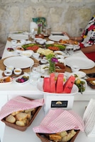 Una mesa dispuesta con diversos platos, incluyendo pan, sandía y una variedad de recipientes y fuentes pequeños.
