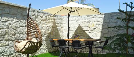 Un patio con un muro de piedra, una silla colgante, una mesa con sillas y una sombrilla.