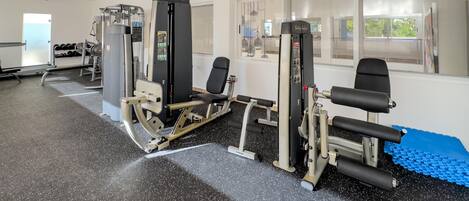 A gym with various exercise machines, a ceiling fan, and a window with a view of greenery.
