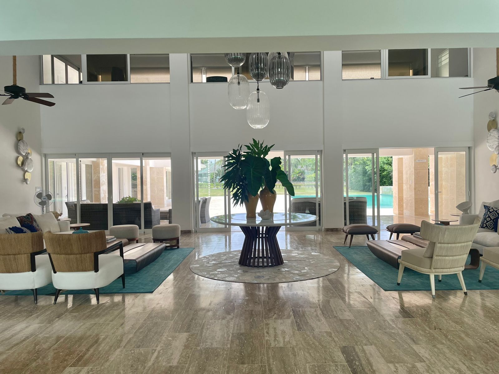 A spacious living room with a central coffee table, comfortable seating, large windows, and a view of a pool.