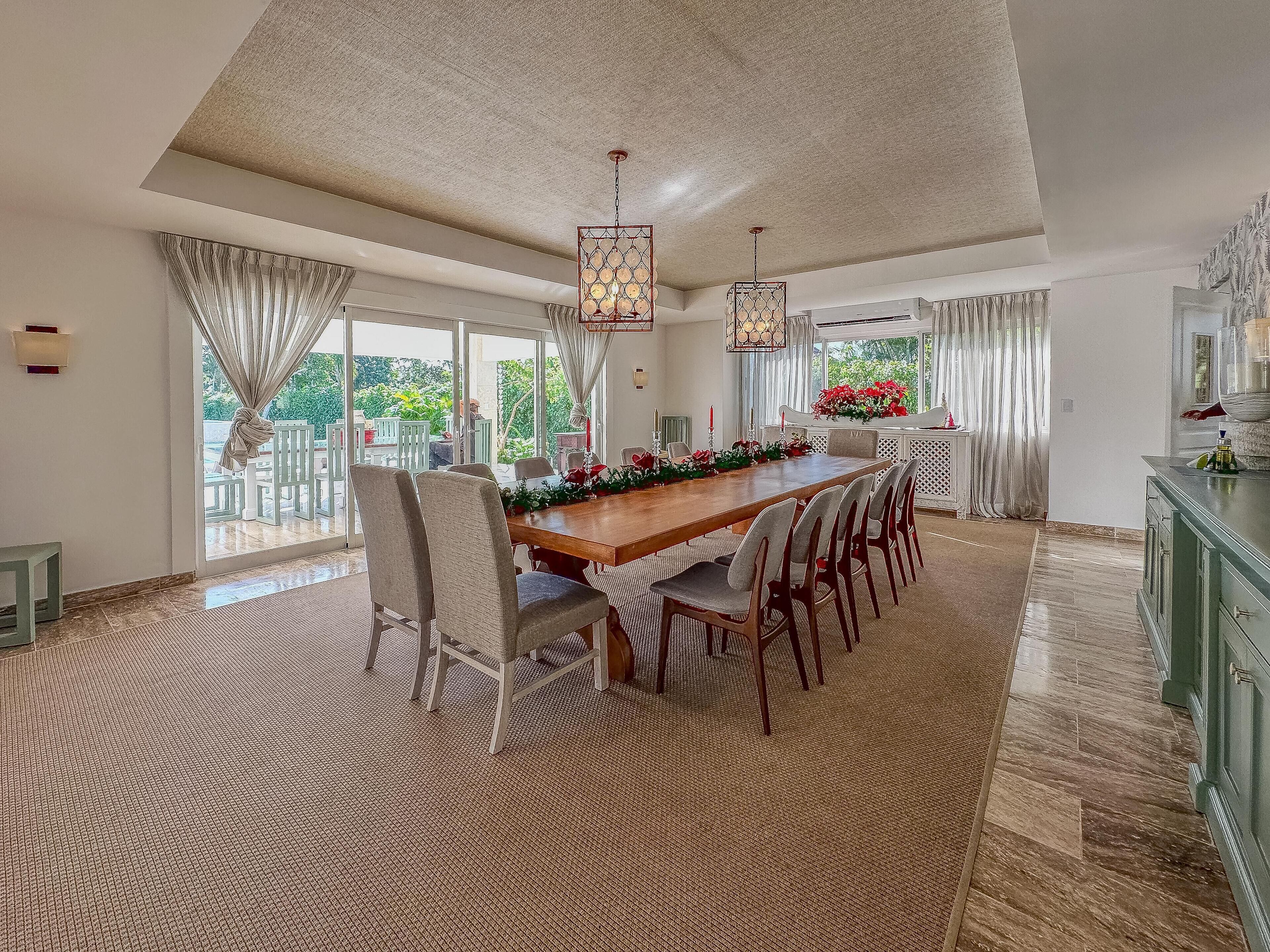 A spacious dining area with a long wooden table, multiple chairs, and hanging pendant lights.