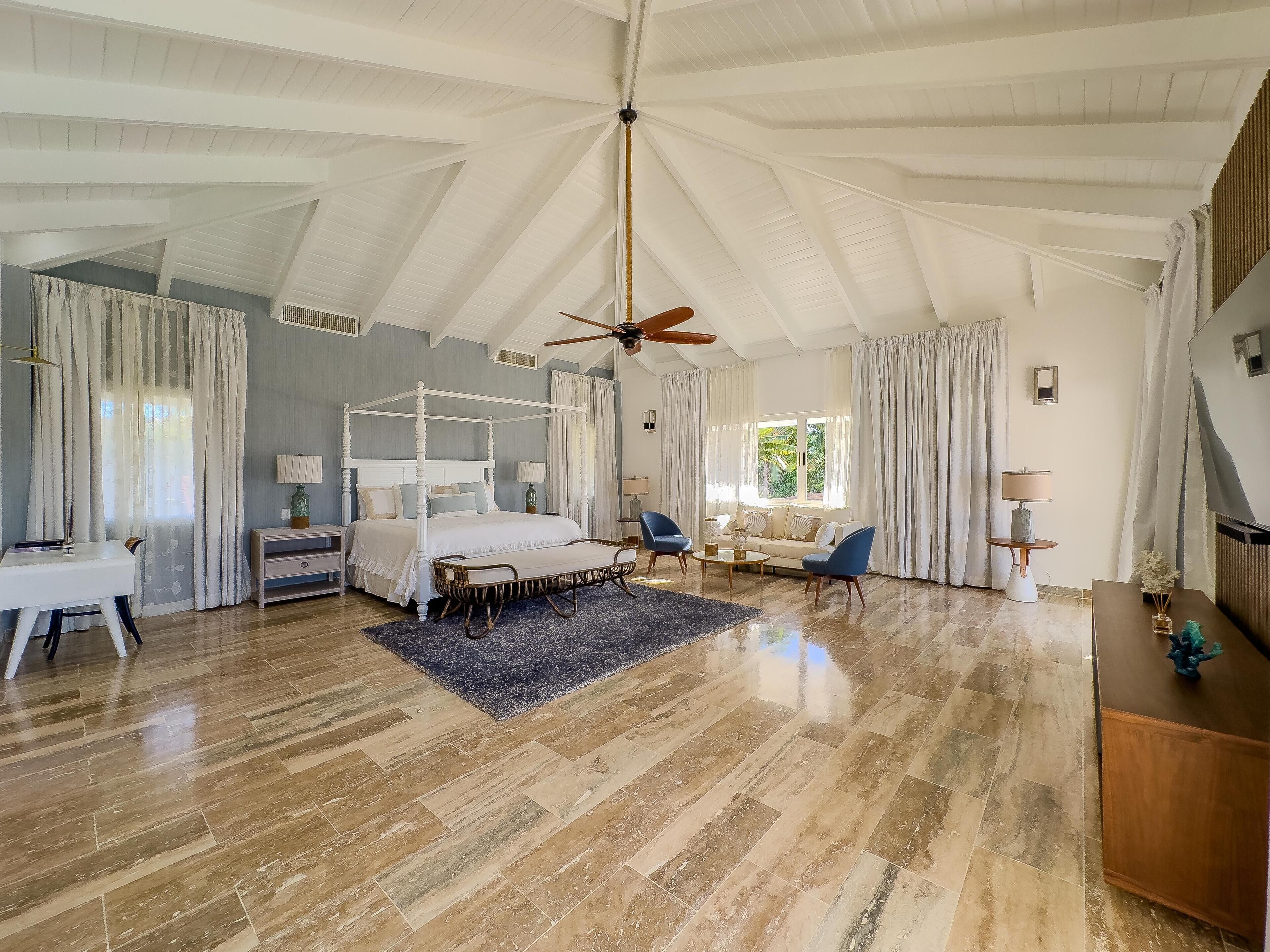 A spacious bedroom with a four-poster bed, a ceiling fan, and a large window with curtains.