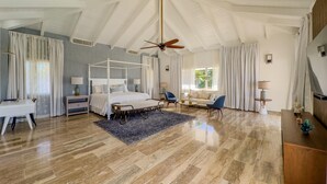Ein geräumiges Schlafzimmer mit einem Himmelbett, Deckenventilator und einem großen Fenster mit Vorhängen.