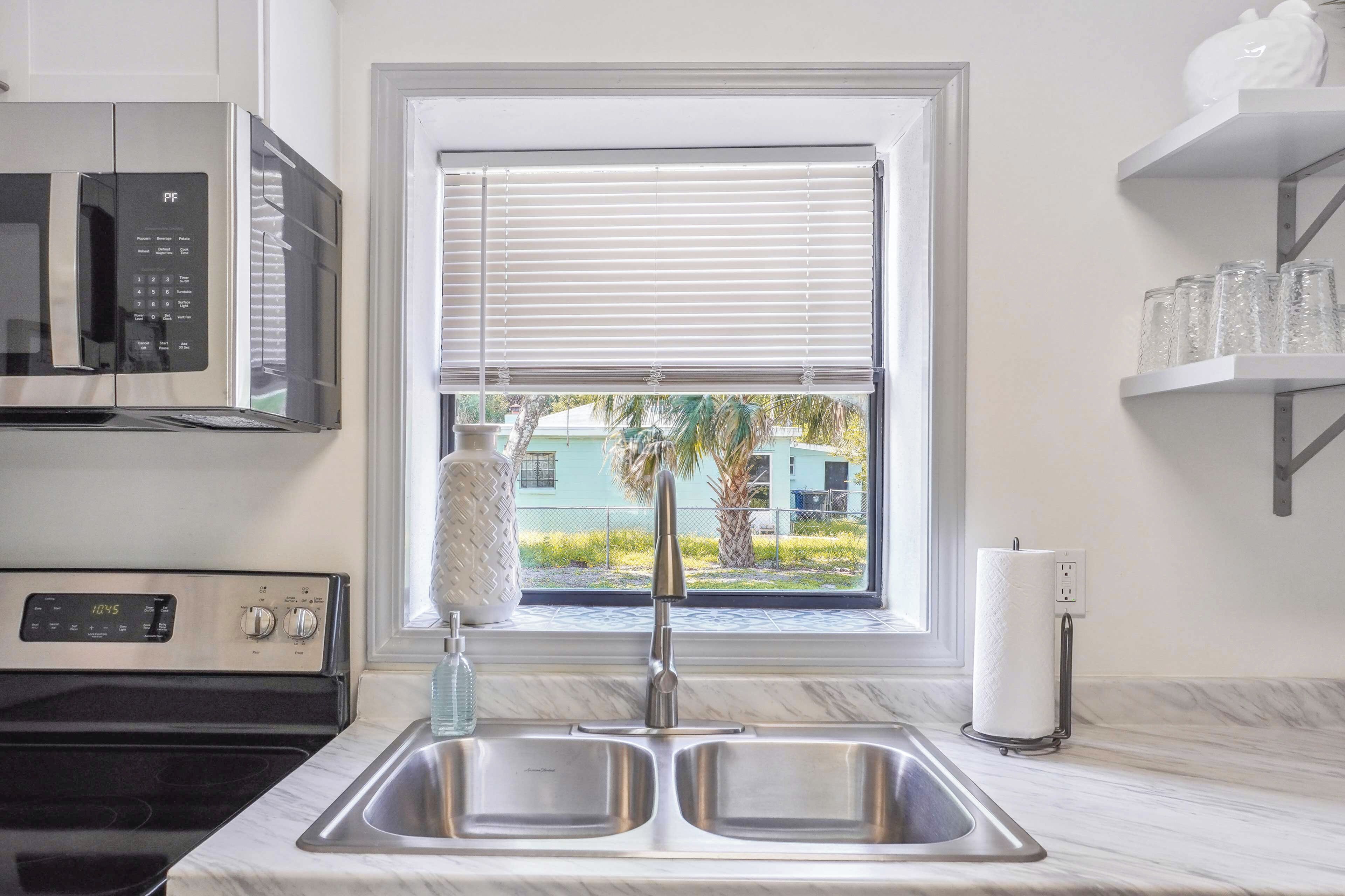 A kitchen with a double sink, a microwave, a stove, and a window with blinds.
